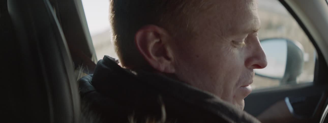 A man looks to his side in the car talking