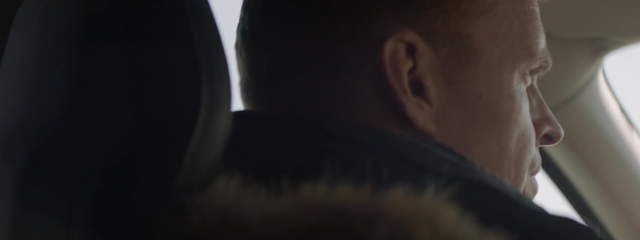 Man in a coat with a fur trimmed hood drives a vehicle