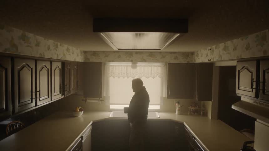 The man holds his mug in the dark kitchen