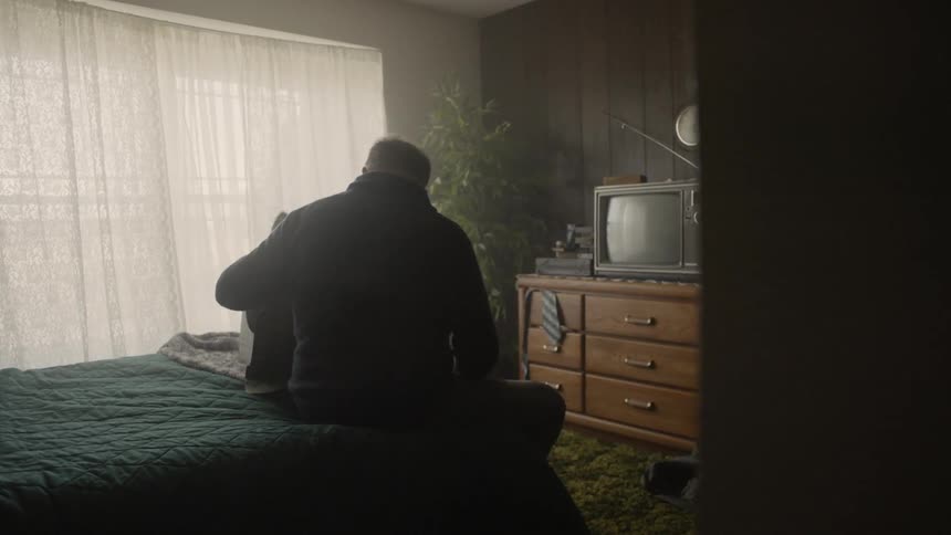 Man sits on a bed looking at things in a box