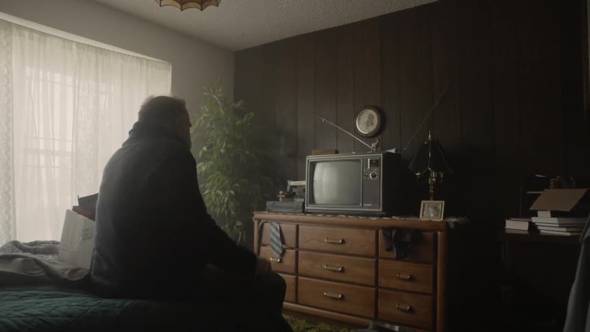 Man sits on the edge of a bed next to a cardboard box