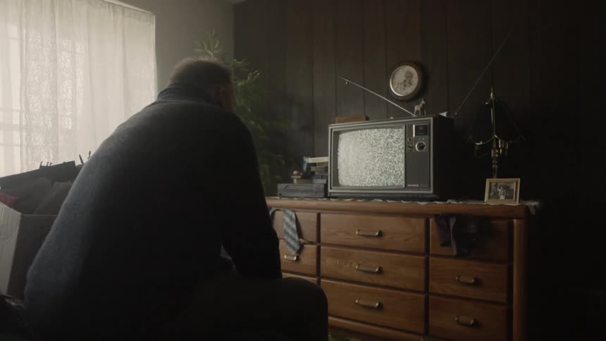 A man leans forward watching a flickering television
