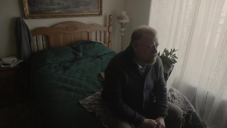A man sits on his bed with his hands clasped
