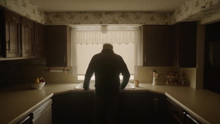 A man leans against his sink in the dark kitchen