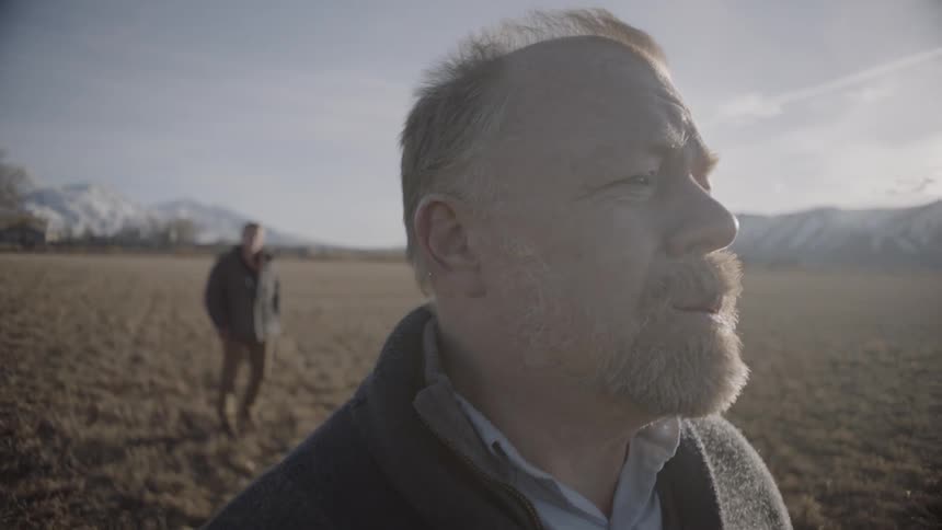 Two men stand in a large field on a sunny day