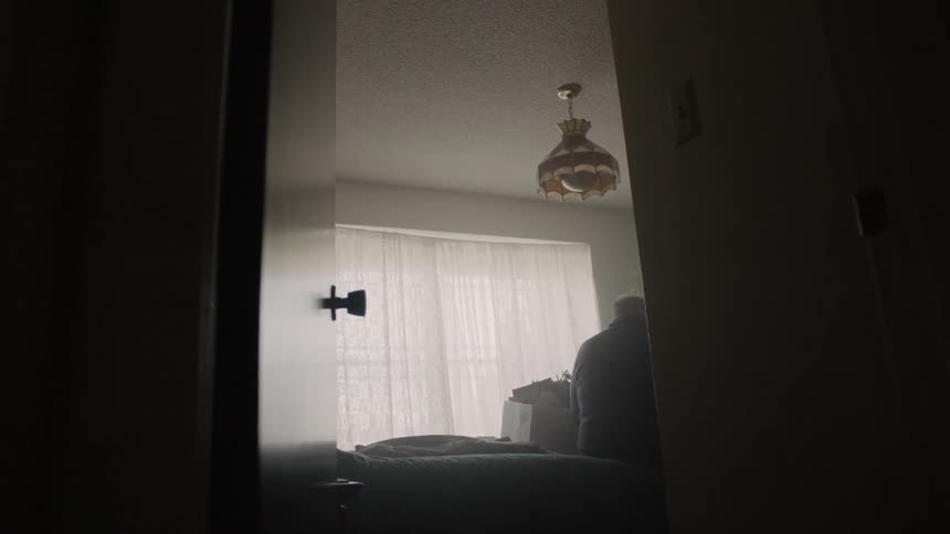 An elderly man sits on the bed