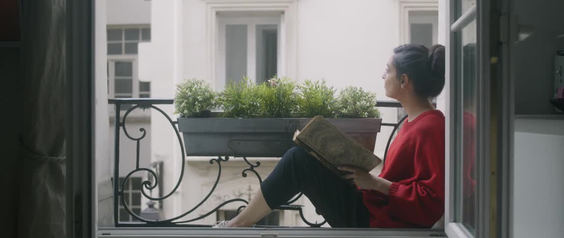 A woman sits reading a book on her window sill