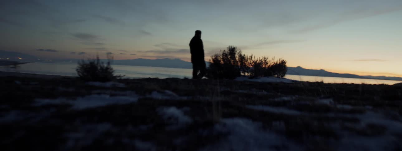 A man is walking near the shore at sunset