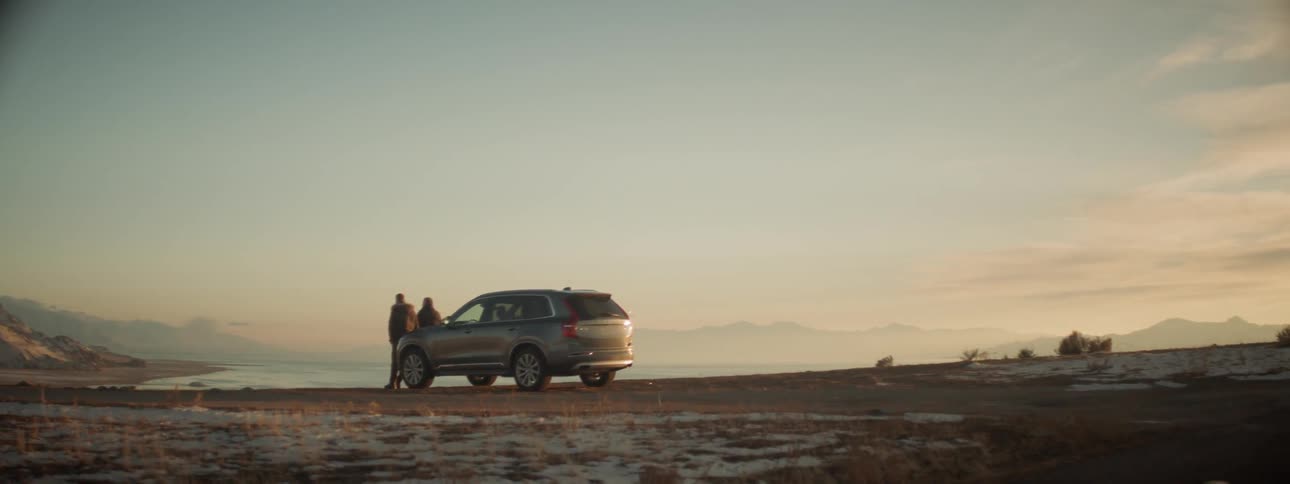 Two men stand in front of a parked suv at sunset
