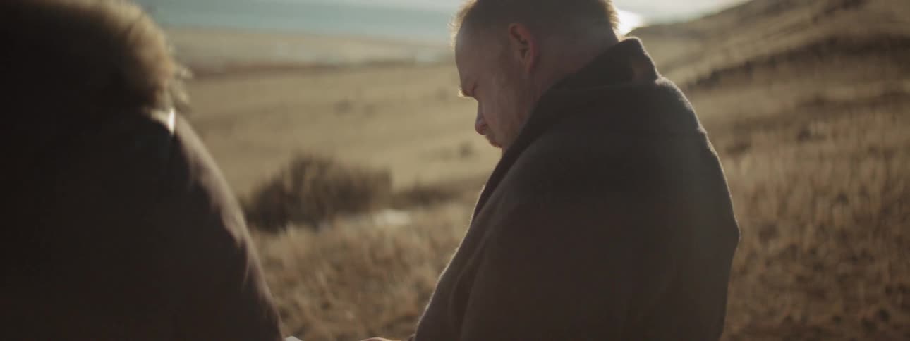 A man is looking at an envelope in his hands before talking to someone