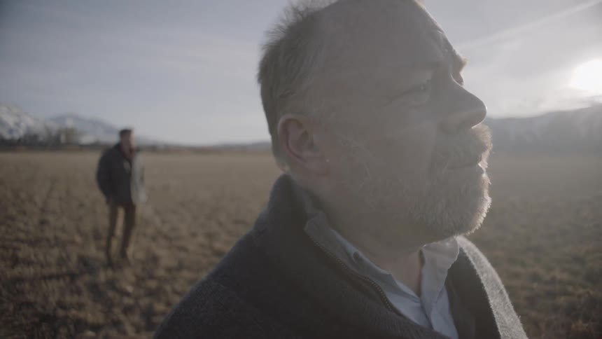 Two men stand in a rural field