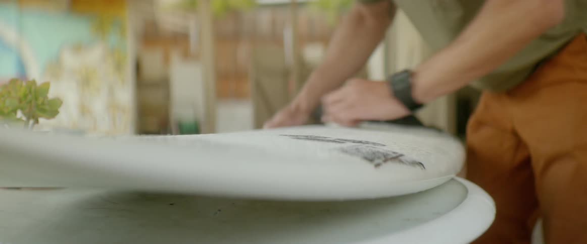 A man is polishing his surfboard in his yard