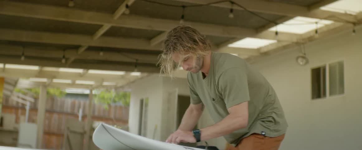 A man waxes his surfboard then carries it away
