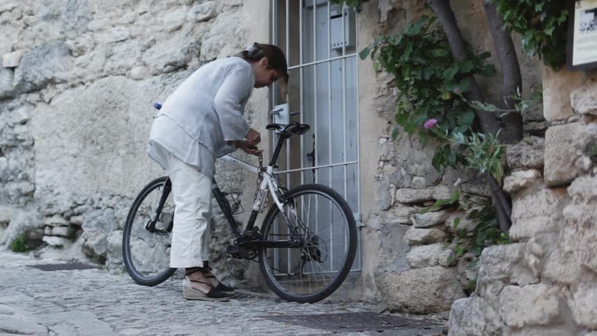 Woman unlocks a bicycle next to a stone building