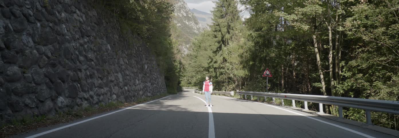 A woman stands alone on the white line in the middle of the road