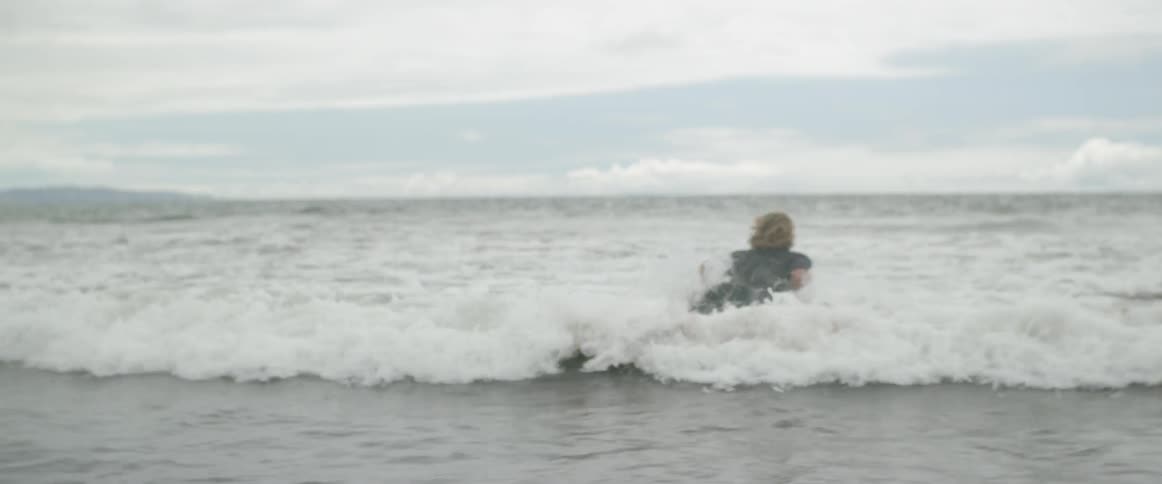A man jumps on his surfboard entering the water