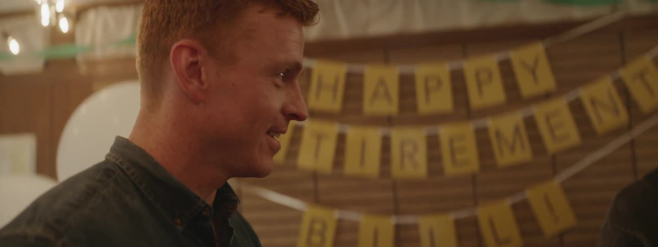 Young man talks to an older man as they stand in front of a happy birthday sign