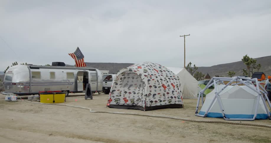 The tents lead up to the silver trailer in the desert
