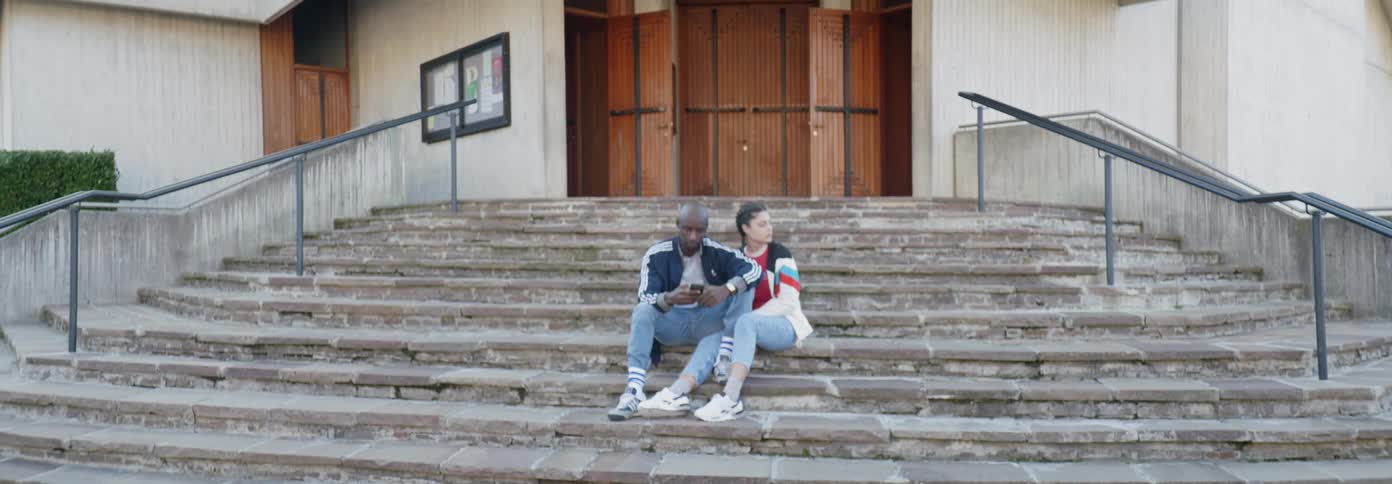A man and woman sit on the steps in front of a building