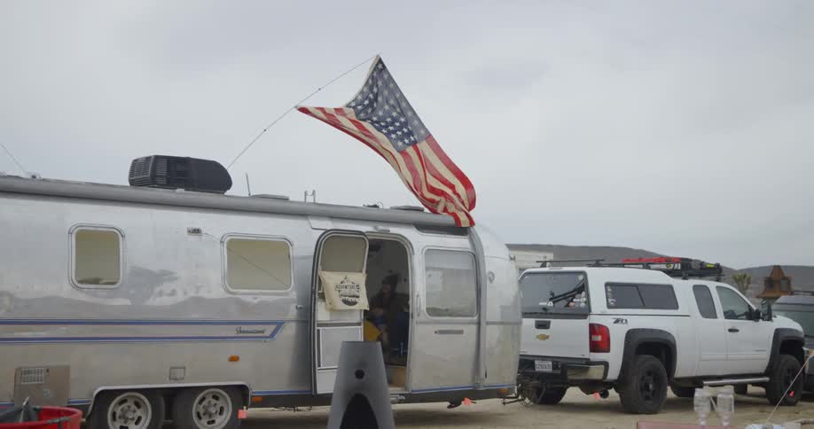 The flag blows in the wind above the silver trailer