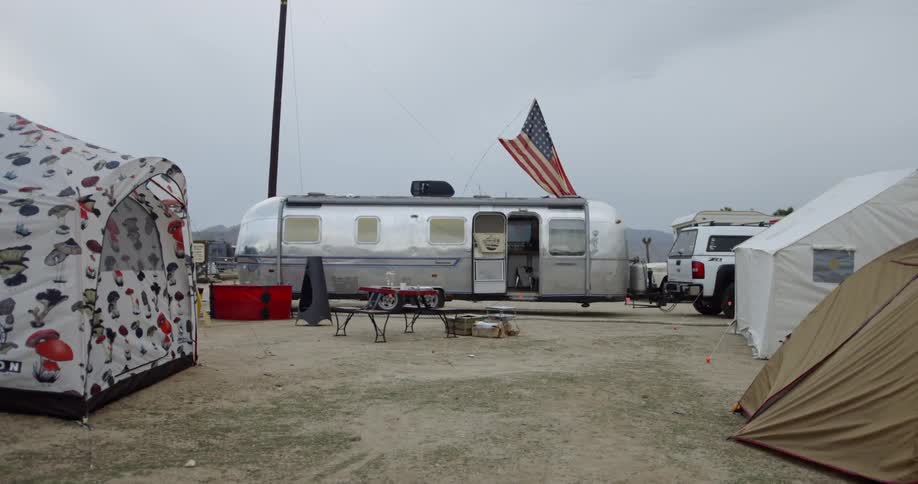 A trailer and tents sit on a campground
