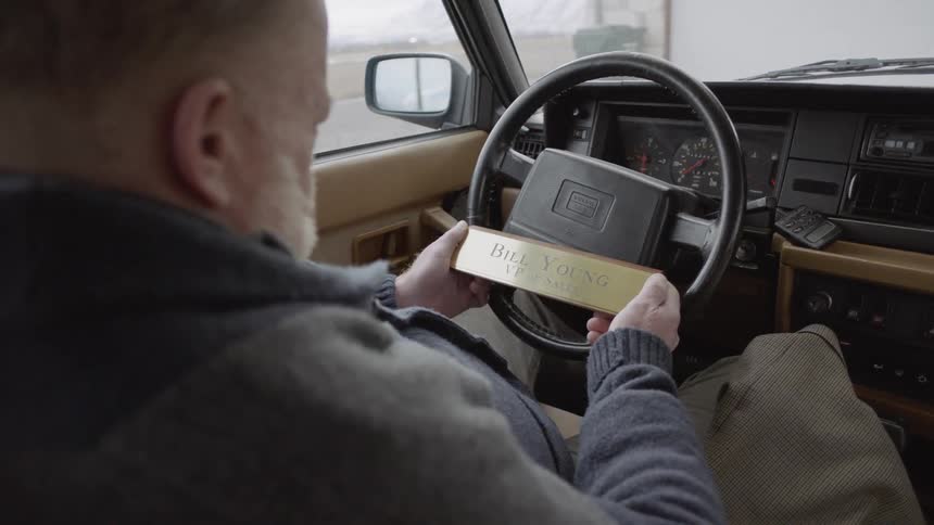 Man sits in a vehicle as he holds a rectangular sign