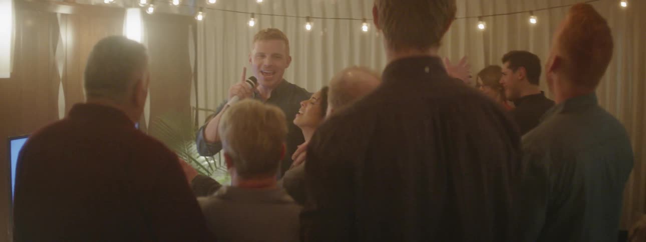 A man sings into the mic at a party full of people