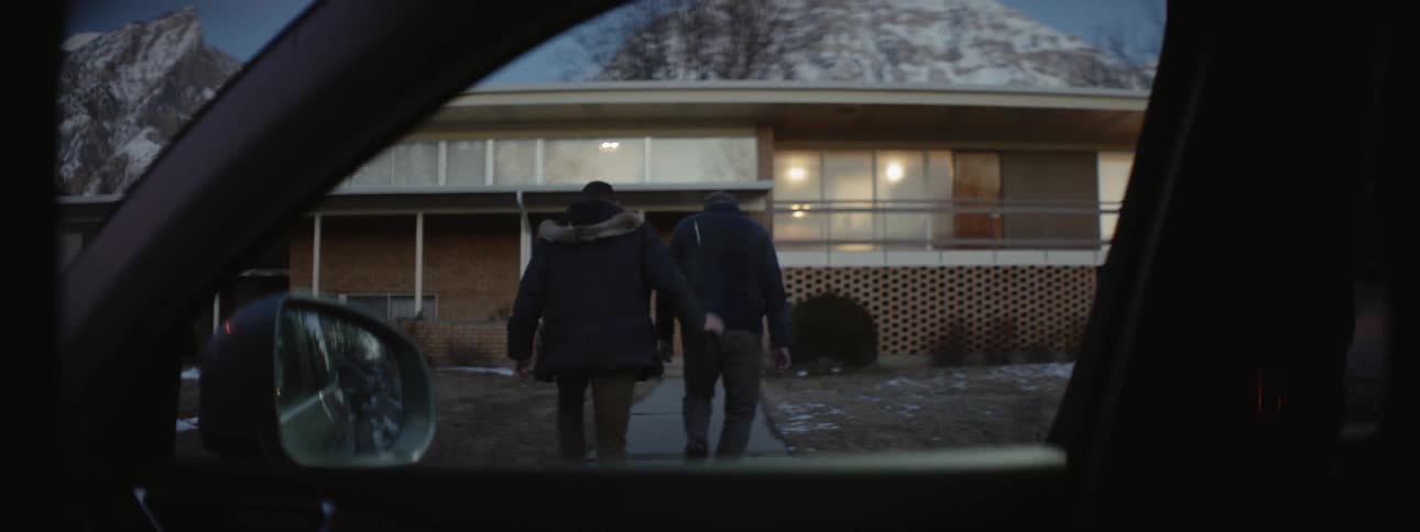 Two men walk on the sidewalk leading up to a house
