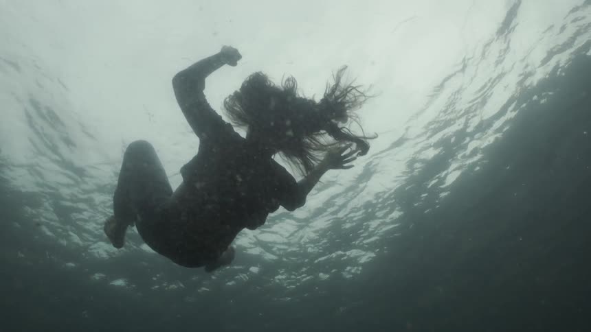 A woman is flapping arms and legs as she falls through the water in daylight