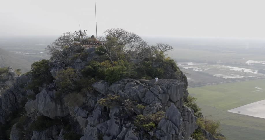 A person stands on top of a rocky ledge overlooking farmland