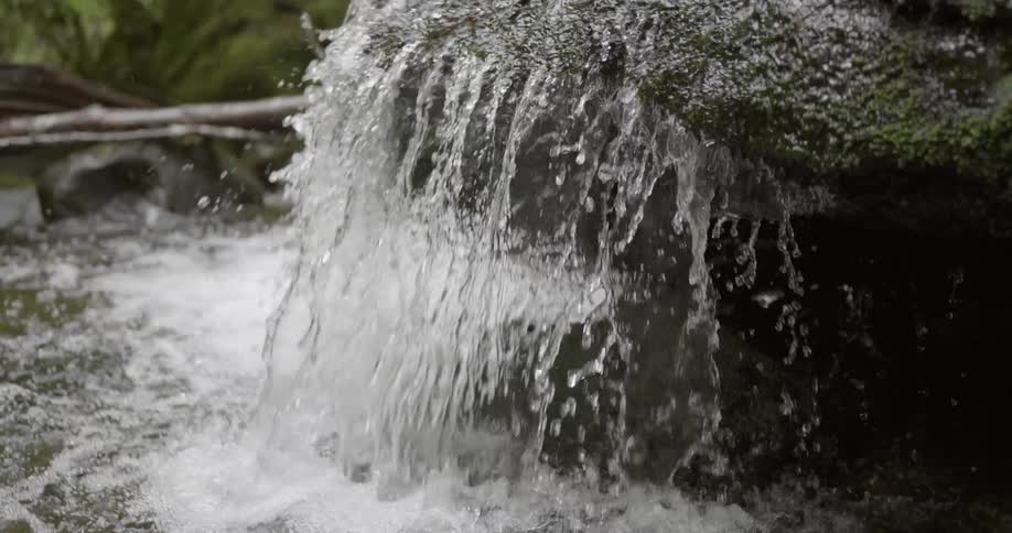 Reveal of a creek being fed by water flowing over a rock above