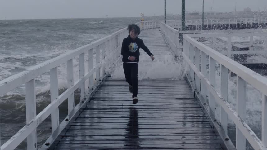 The child races away from the waves hitting the pier