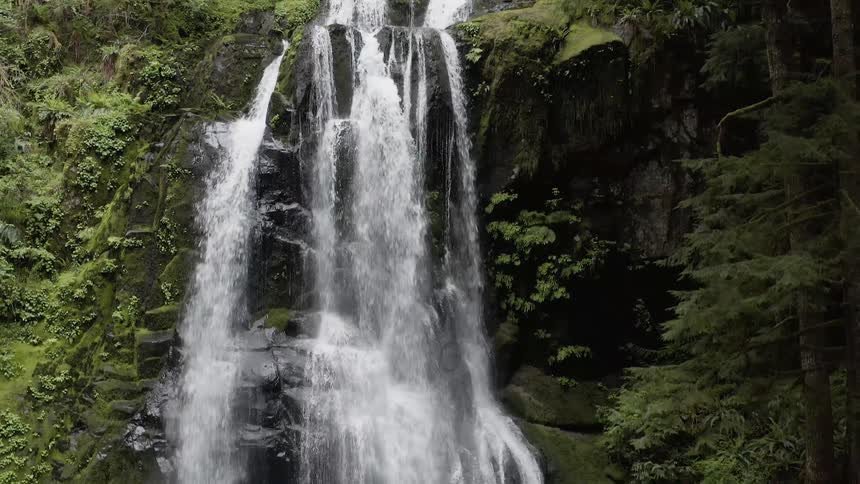 Descending aerial shot of a waterfall rushing over a cliff into a creek below