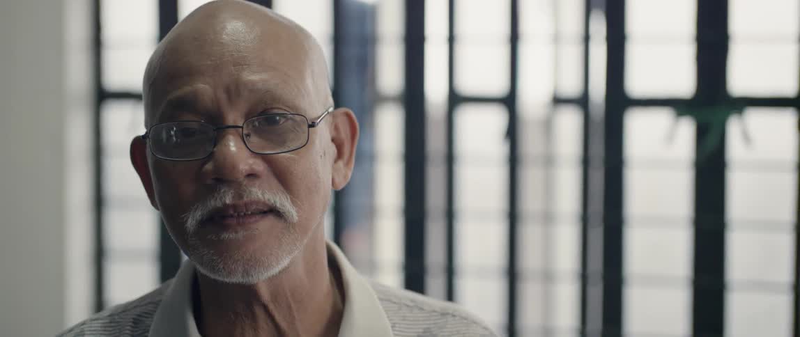 An elderly man sits next to a window