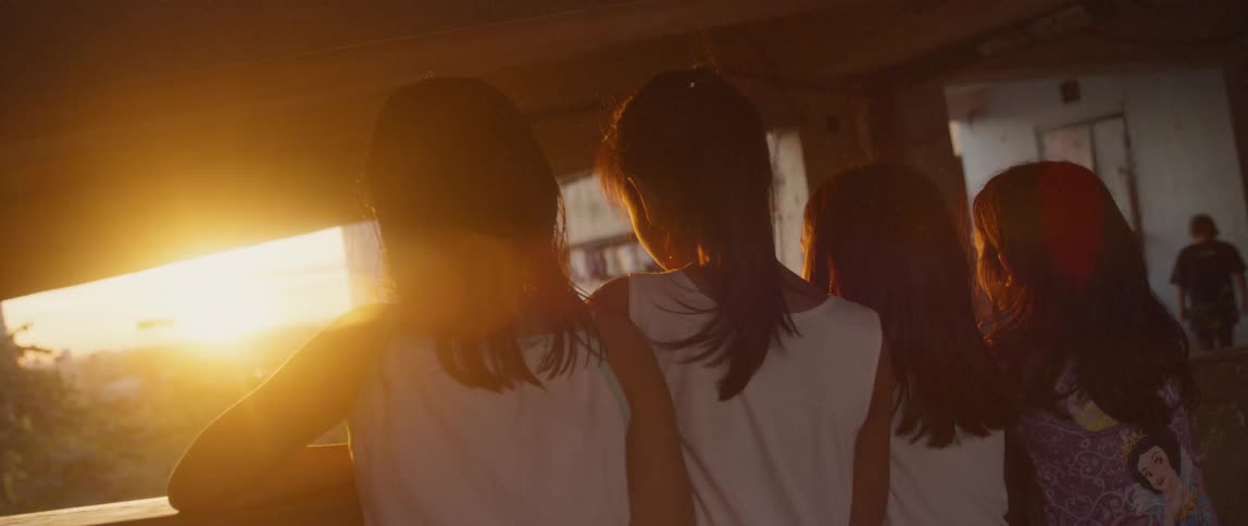 Three girls lean on the wall of a balcony at sunset