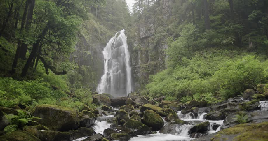 A waterfall flows over a cliff into a stream below