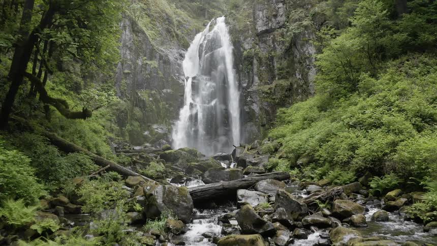 Aerial shot of a cascade flowing into a rocky stream in a green forest