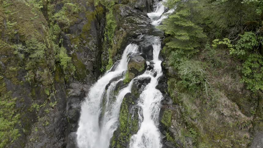 A waterfall in a green forest flows down a cliff 