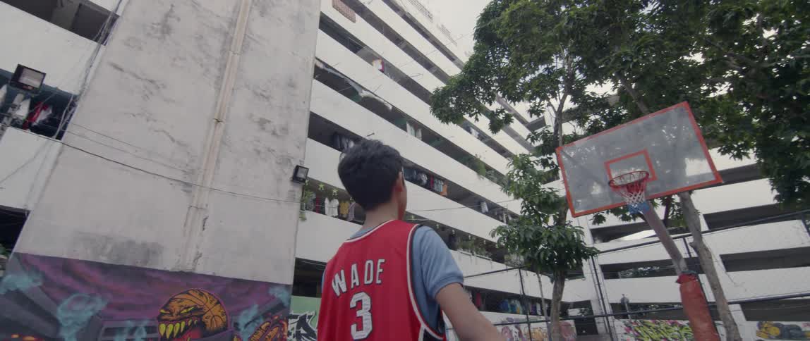 Teenager stands outside on a basketball court holding a ball