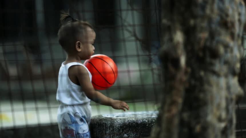 The child is playing with a basketball behind the fence