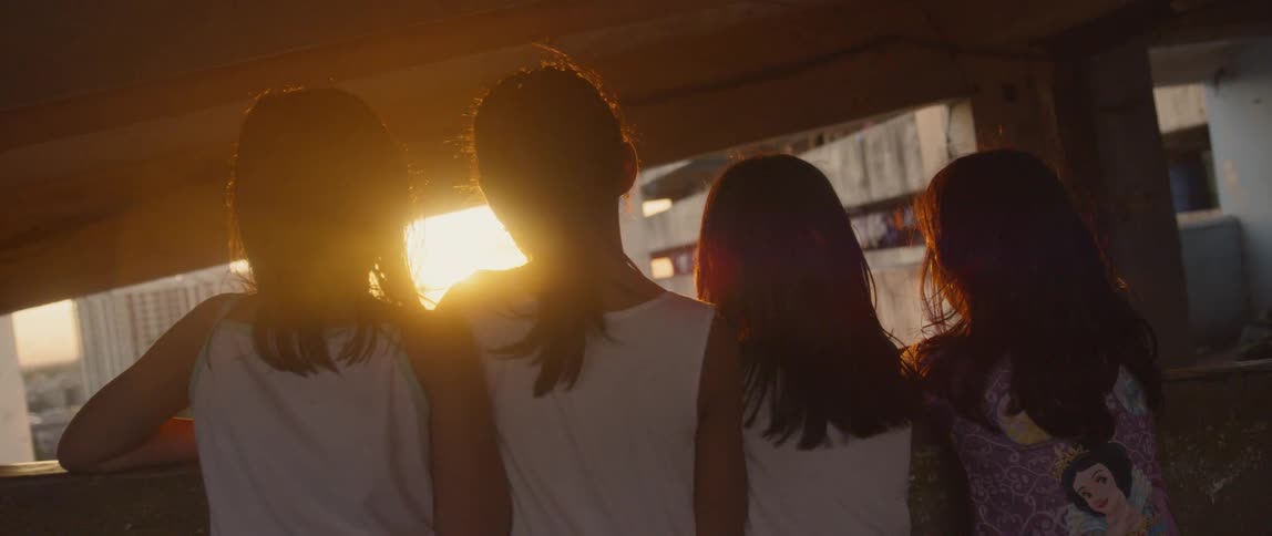 Four young girls stand next to each other as they look out of a window towards the sun