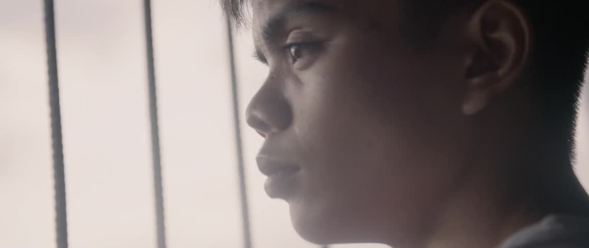 A young boy stands by a barred window