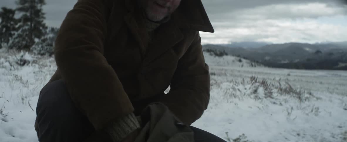 Man on a snowy field searching through a bag pulls out a walkie talkie
