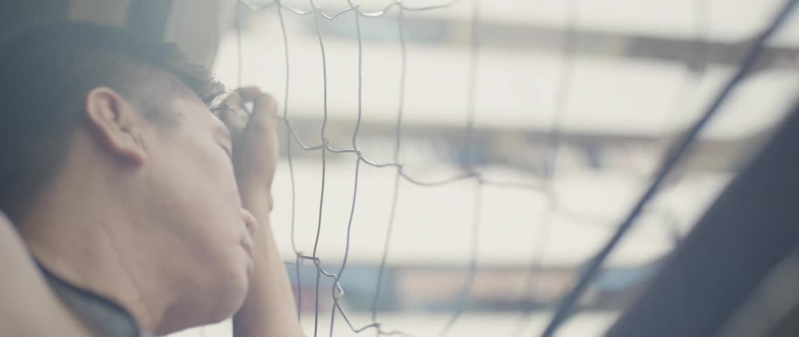 Man hangs onto a wire fence looking through it
