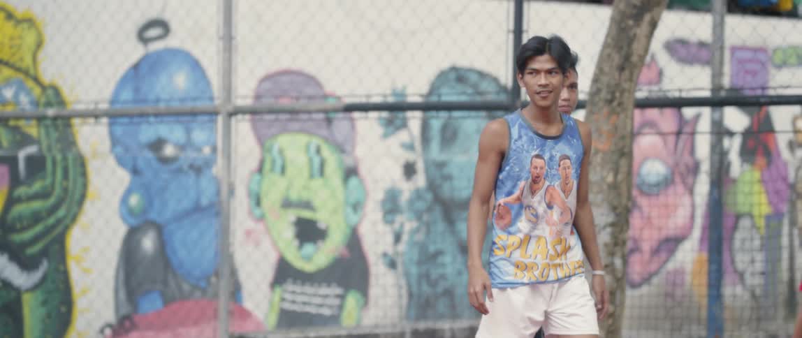 Several children play basketball on a court near a wall filled with graffiti art