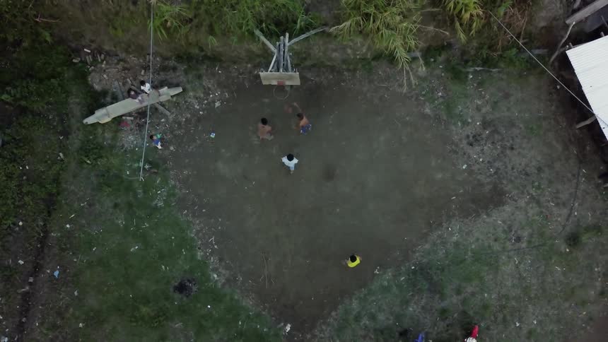 Boys play basketball on a dirt court