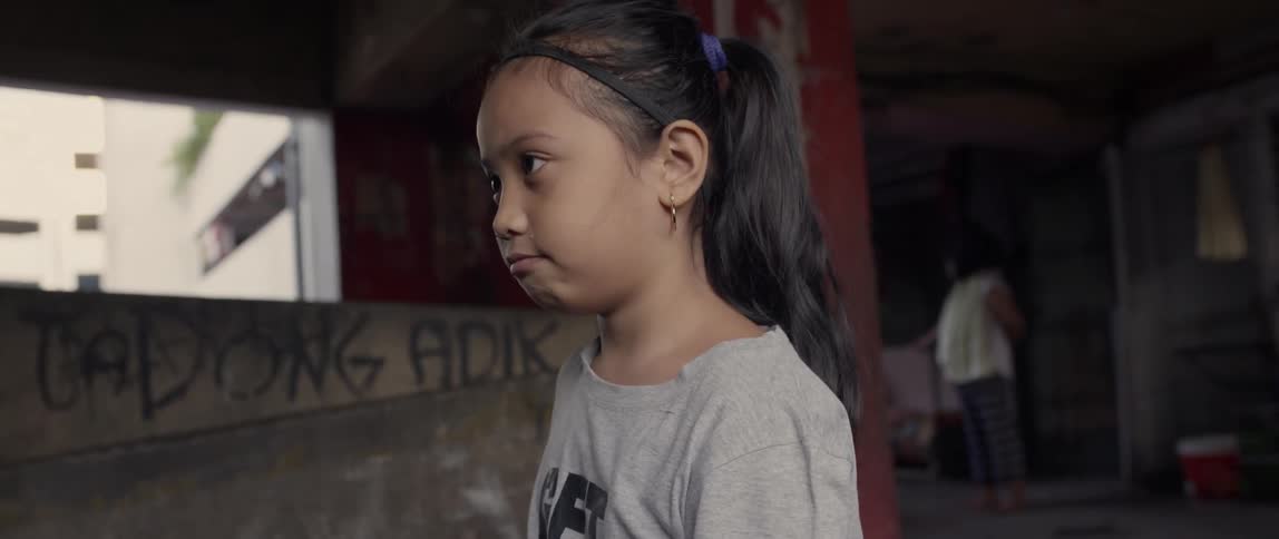 A child looks to her side near the building