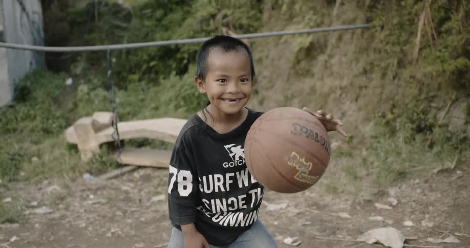 A small child smiles while he bounces a basketball