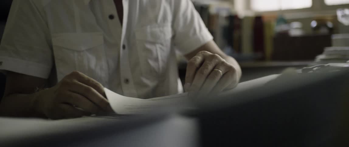 Man with a ring on his finger sits at a table looking at some papers