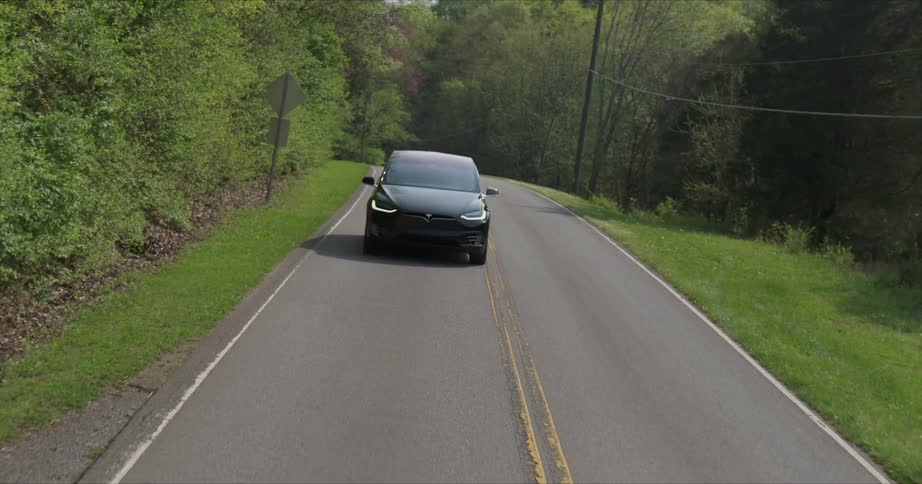 Black car drives down a road surrounded by trees